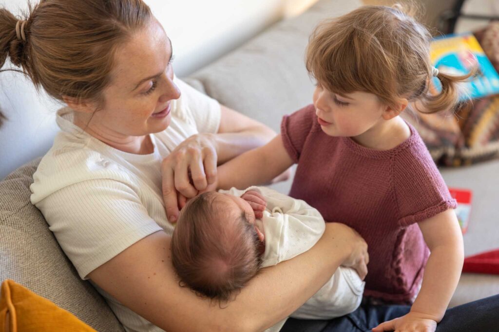 nyfødt baby i mors armer, storesøster klapper på babyen. 