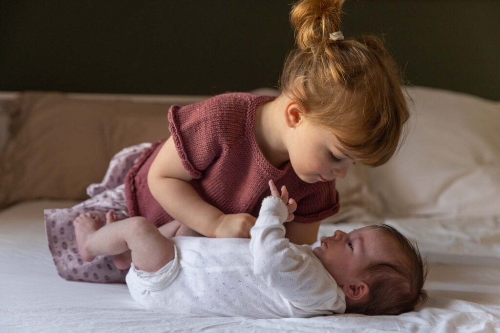 Storesøster lener seg over babyen og leker med henne. 