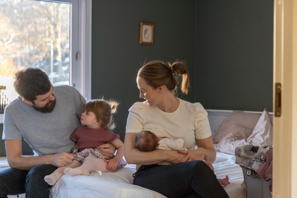 Mor ammer baby mens pappa og storesøster prater sammen.