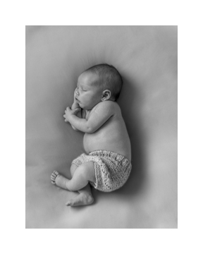Nyfødtfotografering i Bergen av en nyfødt baby som ligger på et teppe - fotografert ovenfra og ned, babyen sover på siden, man ser babyens profil. Har på seg en strikket bleieskjuler og er ellers naken. 